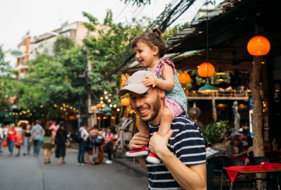 A man carries his young daughter on his shoulders in an outdoor market