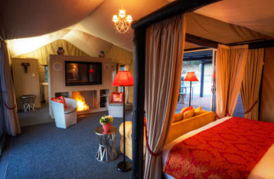 A cozy queen-sized bed, couch, fireplace and entertainment set inside a glamping tent