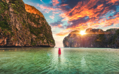 traveller in red paddling in clear waters surrounded by impressive cliff faces.