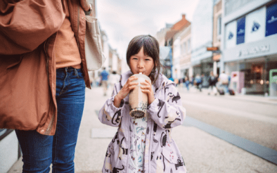 Little girl wearing a purple jacket holding a large cup of bubble tea.