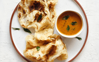 A dish of roti prata served on a white plate with sauce for dipping.