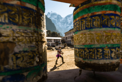A woman is hiking past prayer wheels at Tengboche Monastery, Nepal