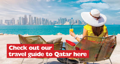 Check out our travel guide to Qatar here | woman drinking an orange juice in a beach chair, looking out over the sea at the city of Qatar