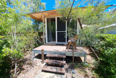 A 2-person glamping cabin set among shrubs under a blue sky.