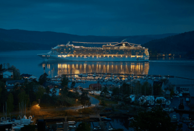 A cruise liner sails into a hilly harbour at night.
