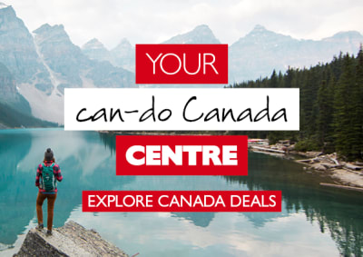 Your can-do Canada centre - explore Canada deals. Hiker standing on a rock looking out at a calm lake with mountains and pine trees in the distance