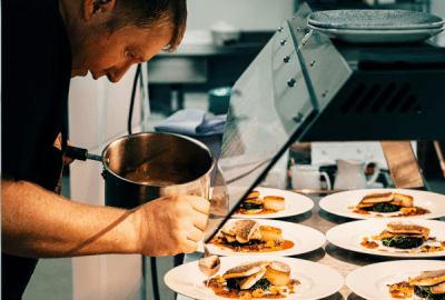 A chef plating meals on white plates from a pot