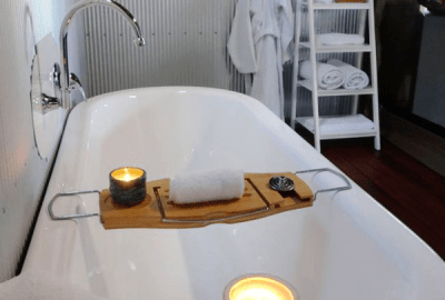 A bath tub with a tray on top filled with hot towel and scented candle