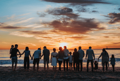 A large group of people gathers on a beach at sunset.