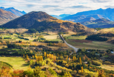 A road runs through green rolling hills with mountains in the background