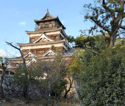 The large wooden Hiroshima Castle nestled among trees in the foreground