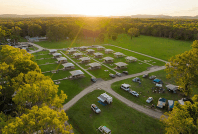 A drone's view of a group of safari tents in a grassy glade at sunset.