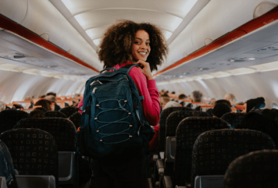 A happy solo woman traveller walks down the aisle inside a plane
