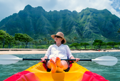 A woman kayaks off the coast Of Hawaii with a forested volcanic range in the background