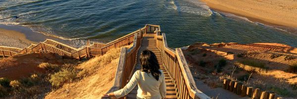 Woman walking down steep wooden steps towards a beach in the late afternoon