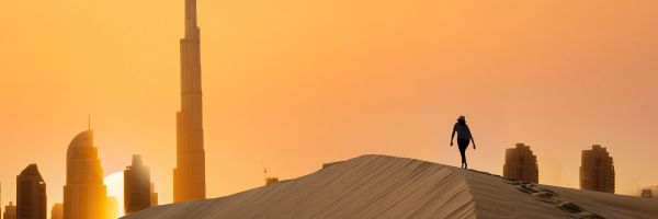 Person walking up dune at sunset with Burj Khalifa in the background