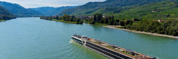 Travelmarvel River Cruise ship sailing past rolling fields and mountains