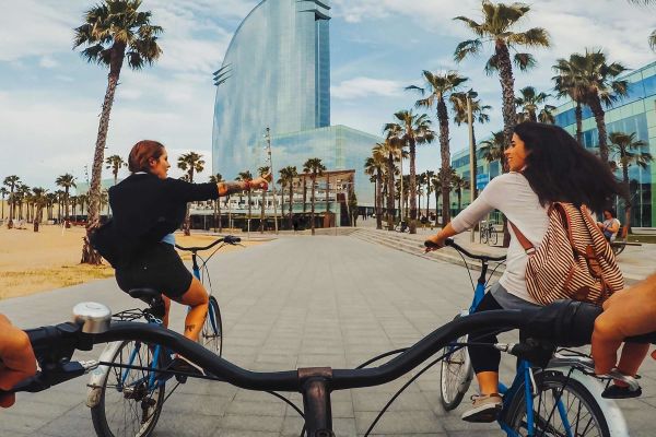 Three people cycling through Barcelona past a beach