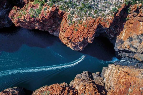 Aerial shot of a boat cruising along red cliffs