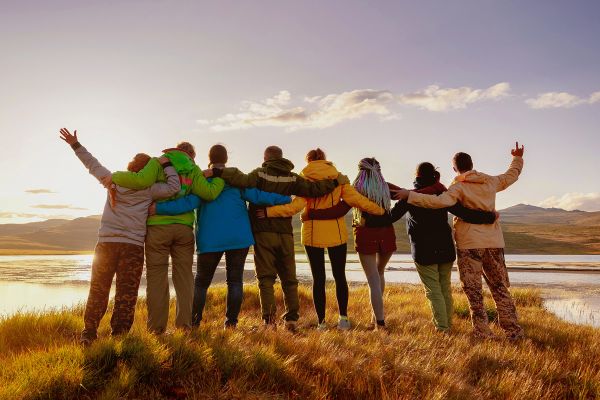 Shot from behind of friends arm in arm watching a sunset from a grassy field