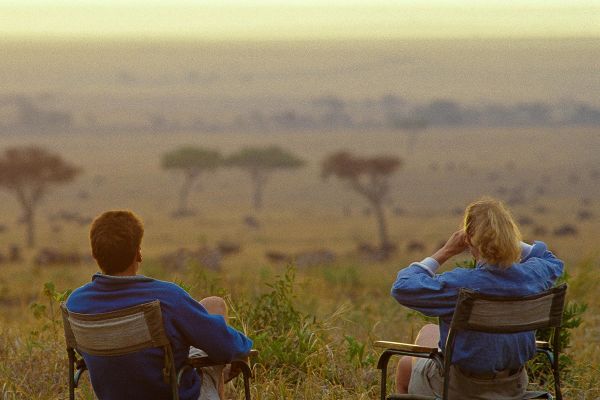 Two people in folding chairs looking out at the savannah