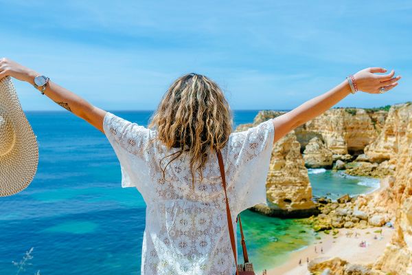 Woman with arms spread looking out over the ocean from a high cliff