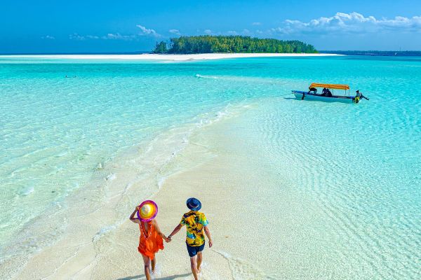 Couple walking hand in hand along a thin strip of sand into a clear blue ocean