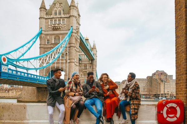 Friends chatting and relaxing on concrete steps with the Tower Bridge in London in the background
