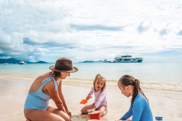 Mother and two girls playing in the sand on a beach with a cruise ship in the background