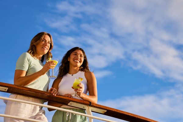 Two ladies drinking cocktails looking over balcony