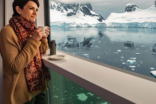 Woman with a hot drink looking out at ice flows from inside a cruise ship