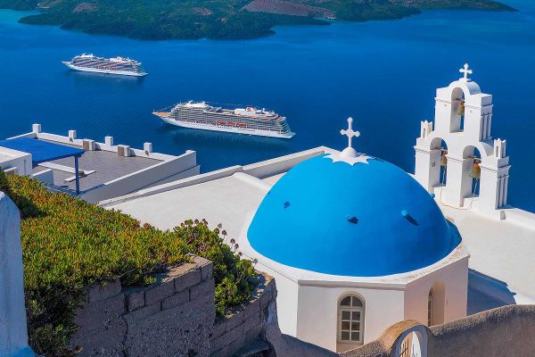 Wide shot of cruise ships at sea framed by blue roofed buildings in Greece