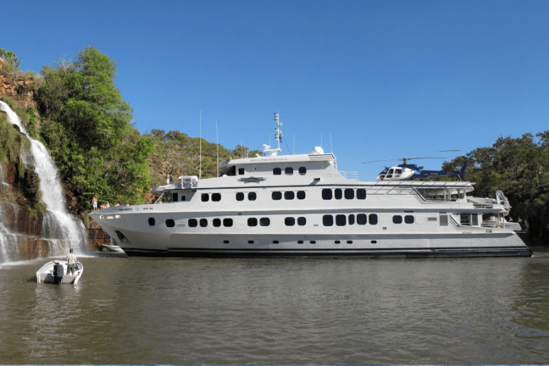 A small cruise ship anchors by a waterfall in Kimberley, Western Australia