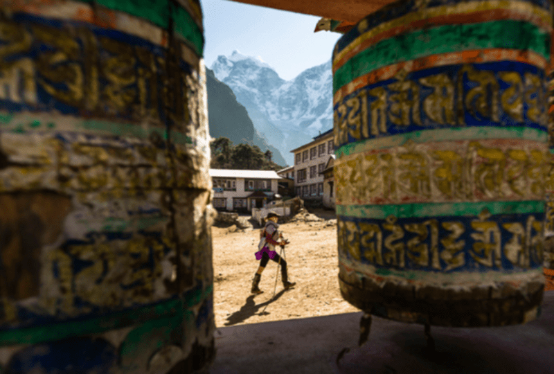 A woman is hiking past prayer wheels at Tengboche Monastery, Nepal