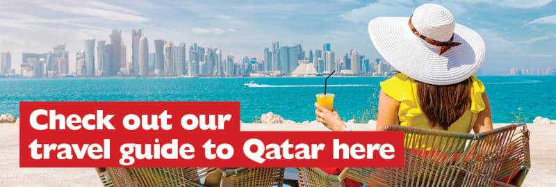 Check out our travel guide to Qatar here | woman drinking an orange juice in a beach chair, looking out over the sea at the city of Qatar