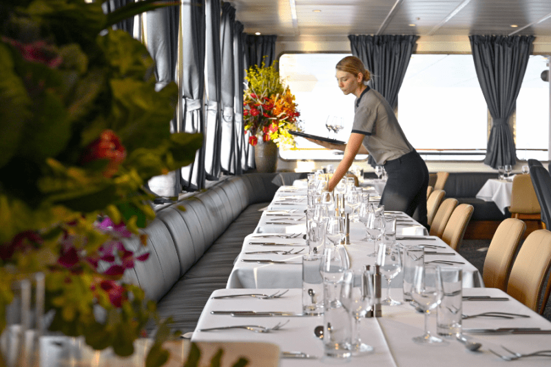 A woman sets places at a dining tables aboard a small cruise ship