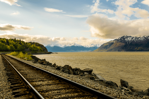 a railway track running beside a vast lake with mountains in the background.